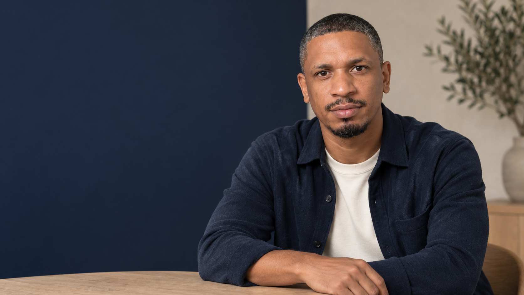 Christopher Da Silva assis face à l’objectif, en surchemise bleu nuit, les bras posés sur une table.